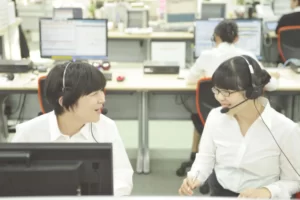2名の女性オペレーターがコンピューターの前で会話しているシーン
