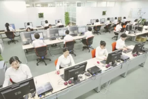オープンプランオフィスでコンピューターに向かって作業している多くの従業員がいる様子